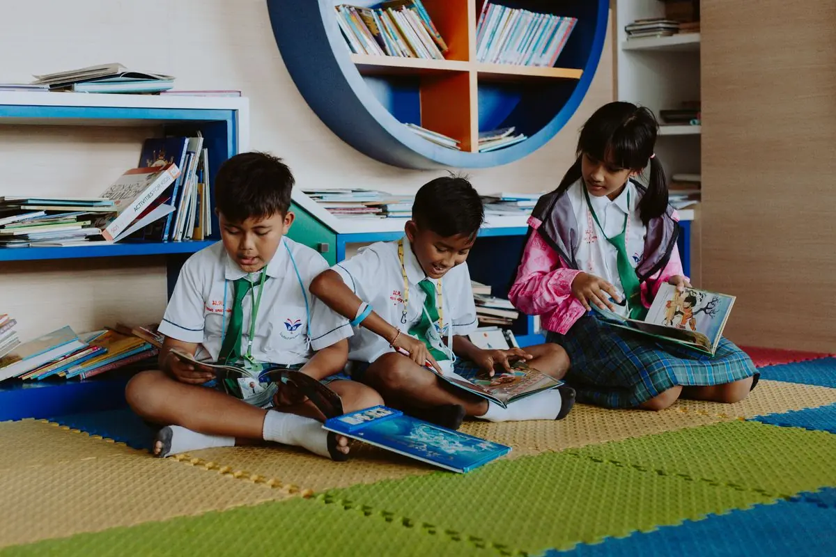 Pupils in uniform reading books together on a colourful library floor