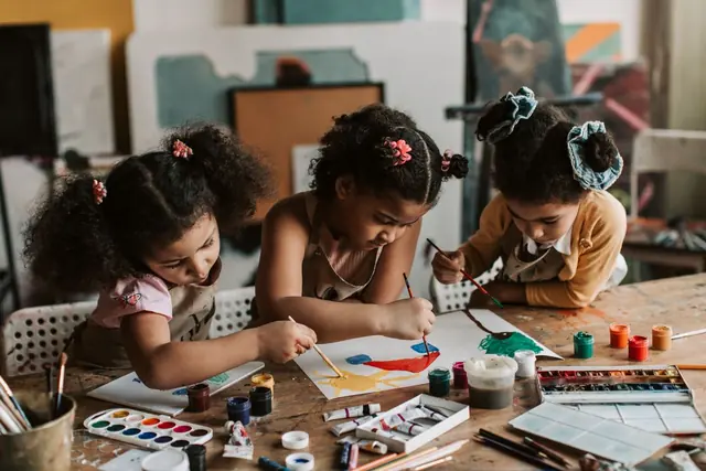 Children painting together at a table covered with art supplies