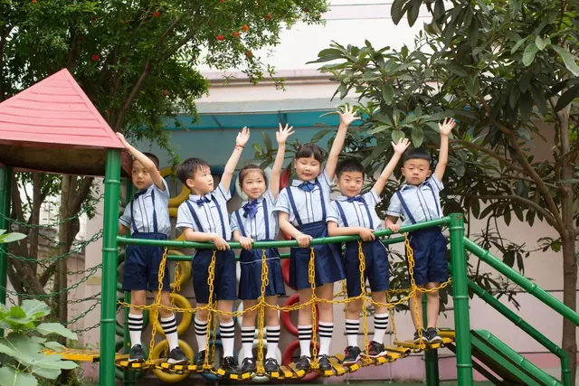 Young pupils in uniform cheering on outdoor play equipment