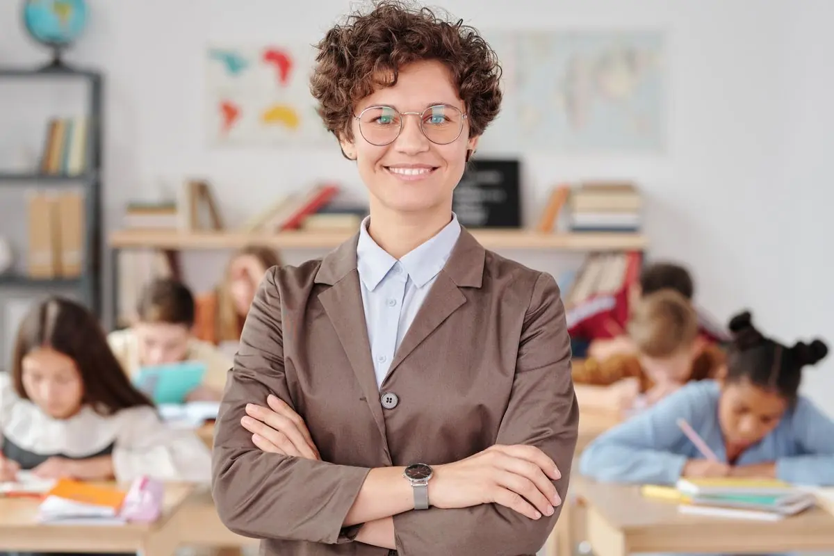 A smiling teacher standing in a classroom while pupils work in the background
