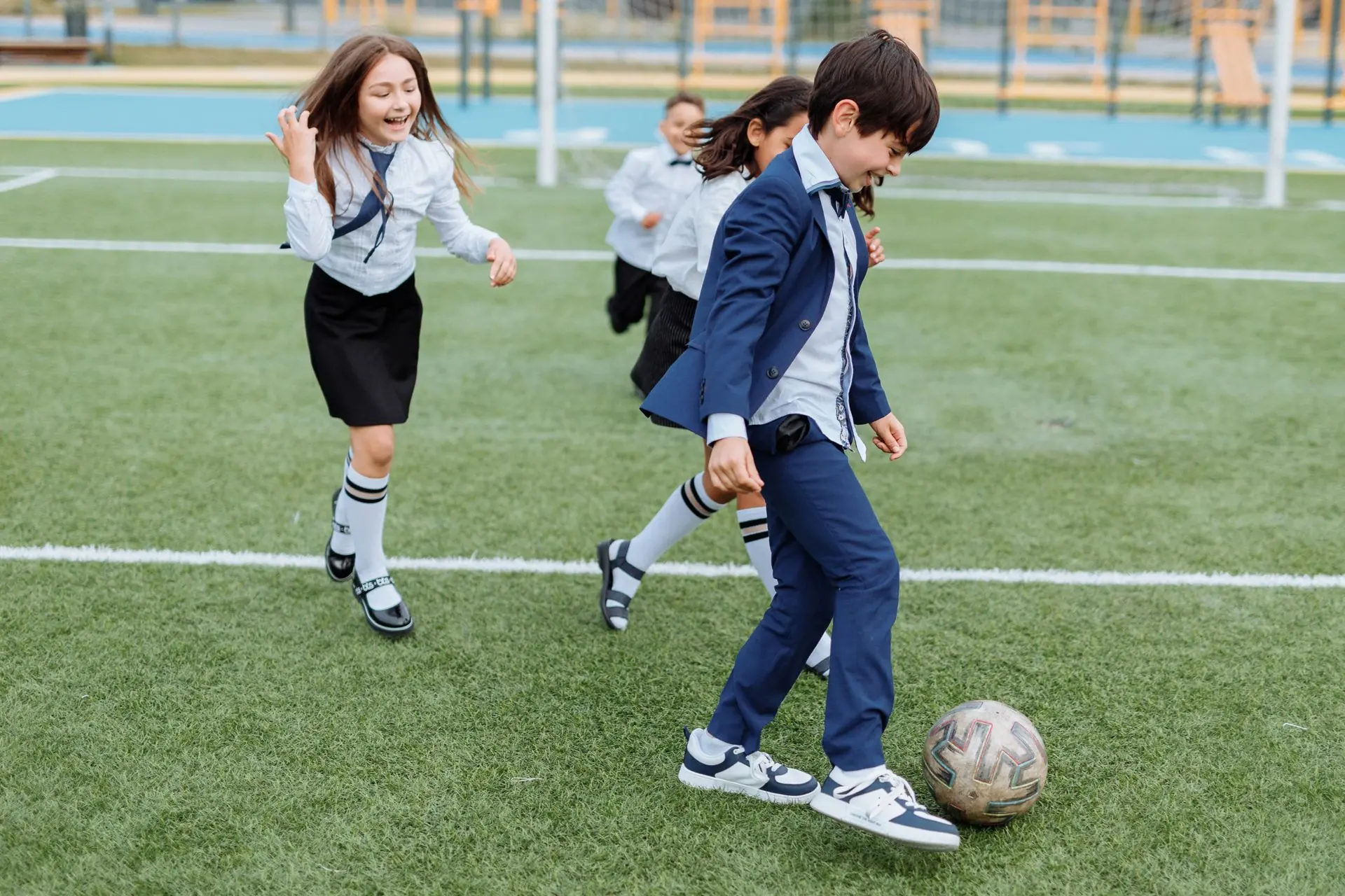 Pupils in school uniform playing football on a green sports field