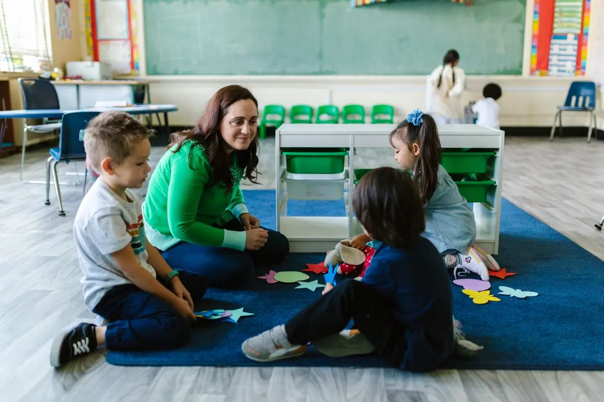 A teacher sitting on the floor with young children during a group activity