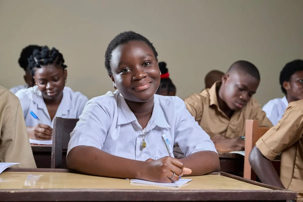A smiling secondary pupil writing at a desk in class
