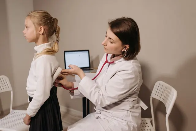 A doctor listening to a young child's back with a stethoscope