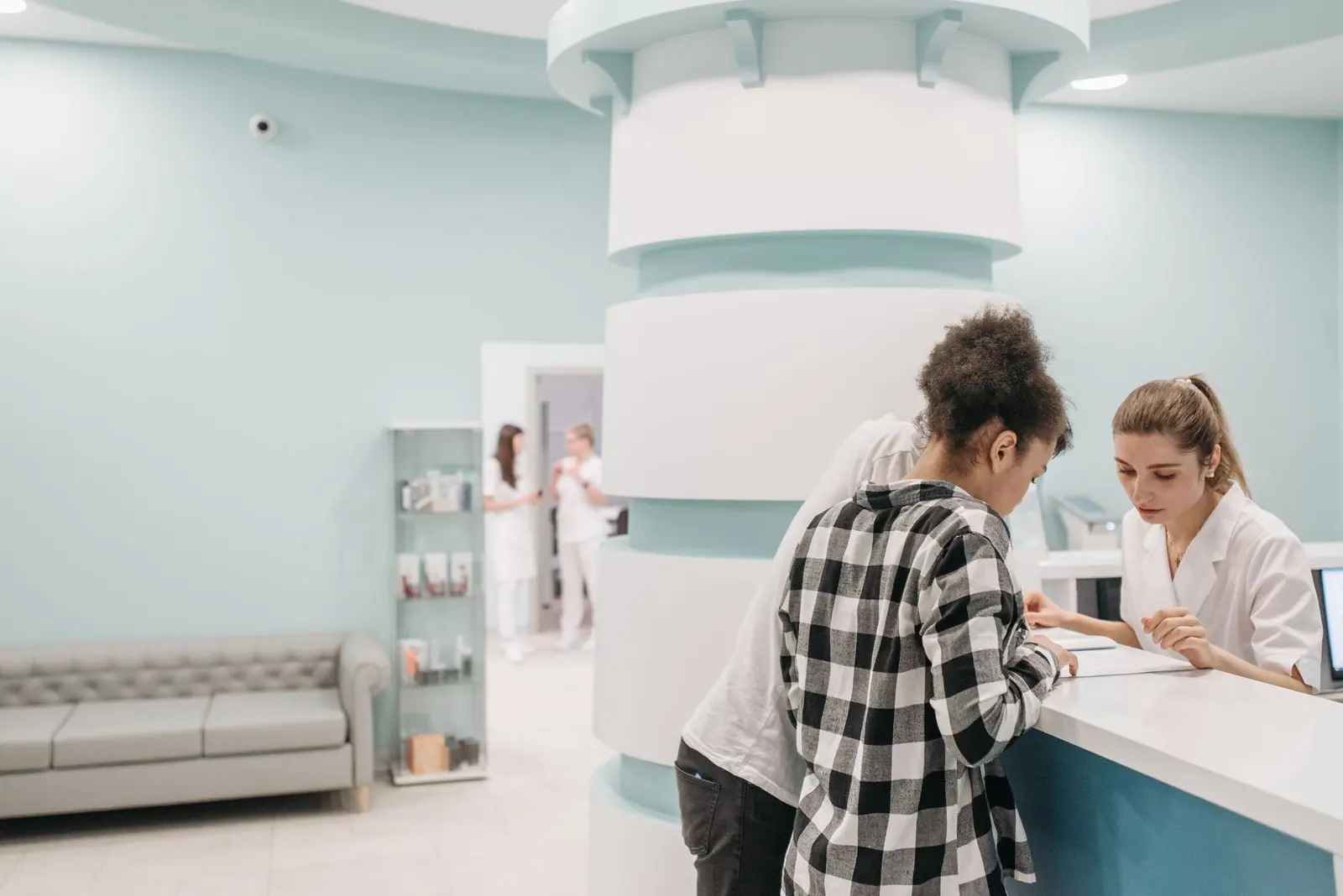A patient speaking with staff at a bright teal and white clinic reception
