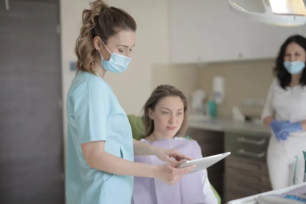 A dental professional speaking with a patient beside a treatment chair