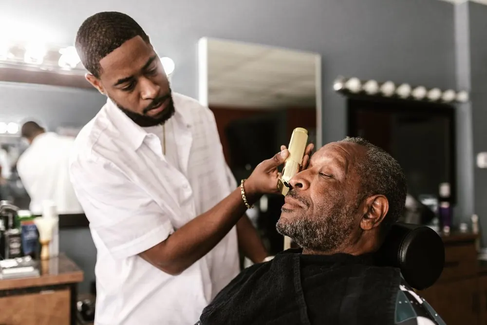 A barber carefully shaping a seated client's haircut