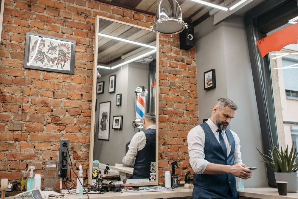 An exposed-brick barbershop with a barber beside a styling station