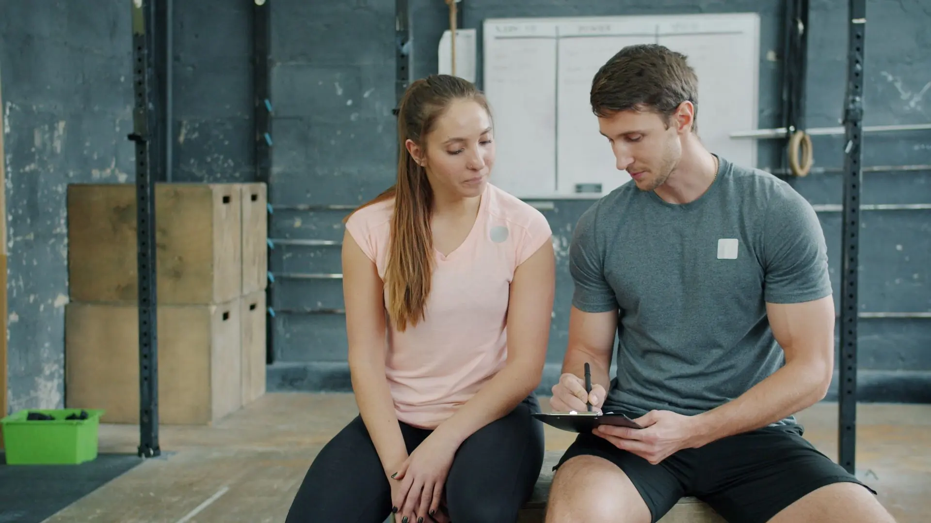 A trainer sitting with a new member and talking through a plan on a clipboard