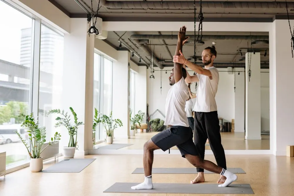 A yoga instructor guiding a participant through a standing lunge in a bright studio