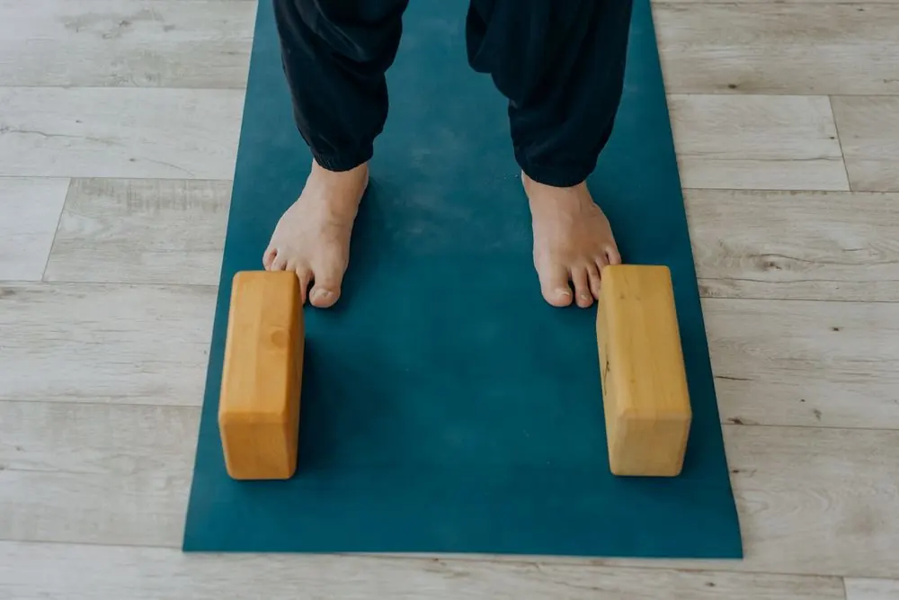 A person placing wooden yoga blocks beside their feet on a mat