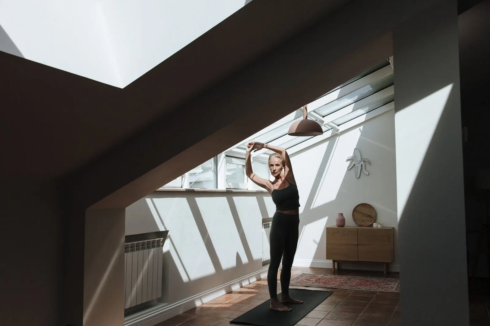 A person stretching on a mat in a sunlit loft studio