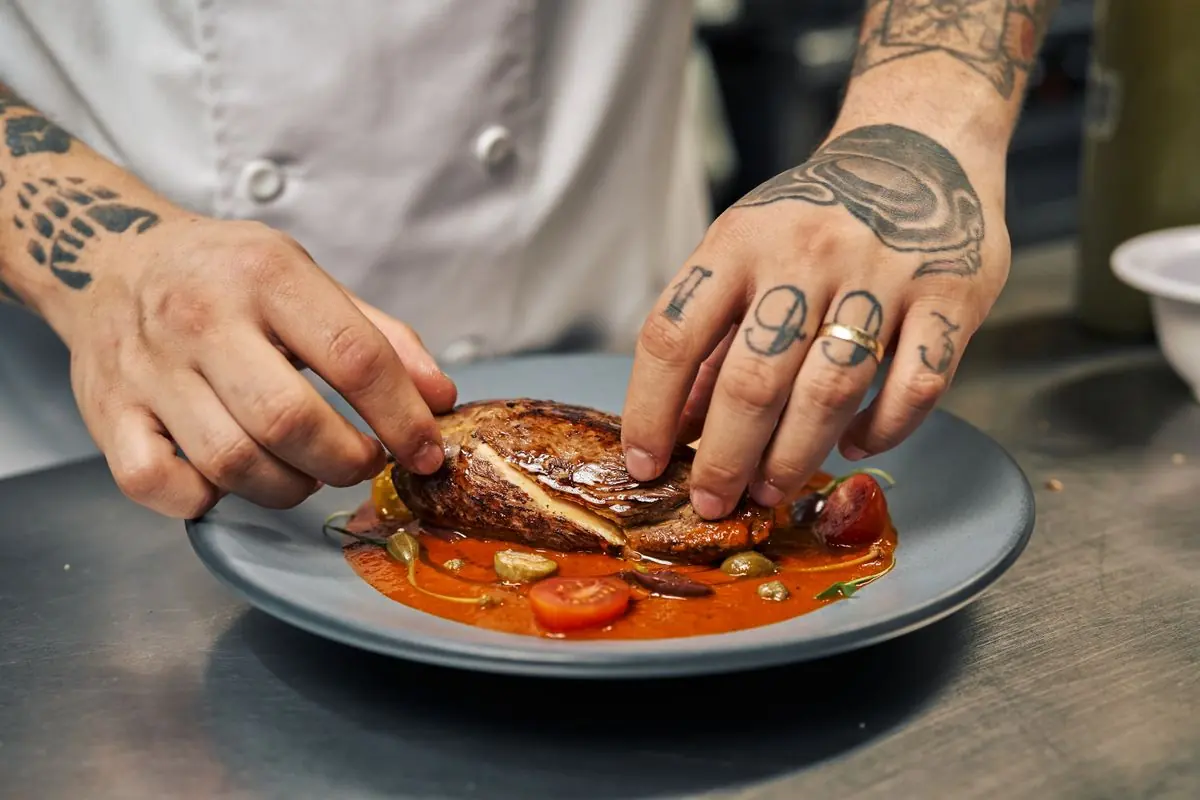 A chef's hands carefully plating a dish with sauce