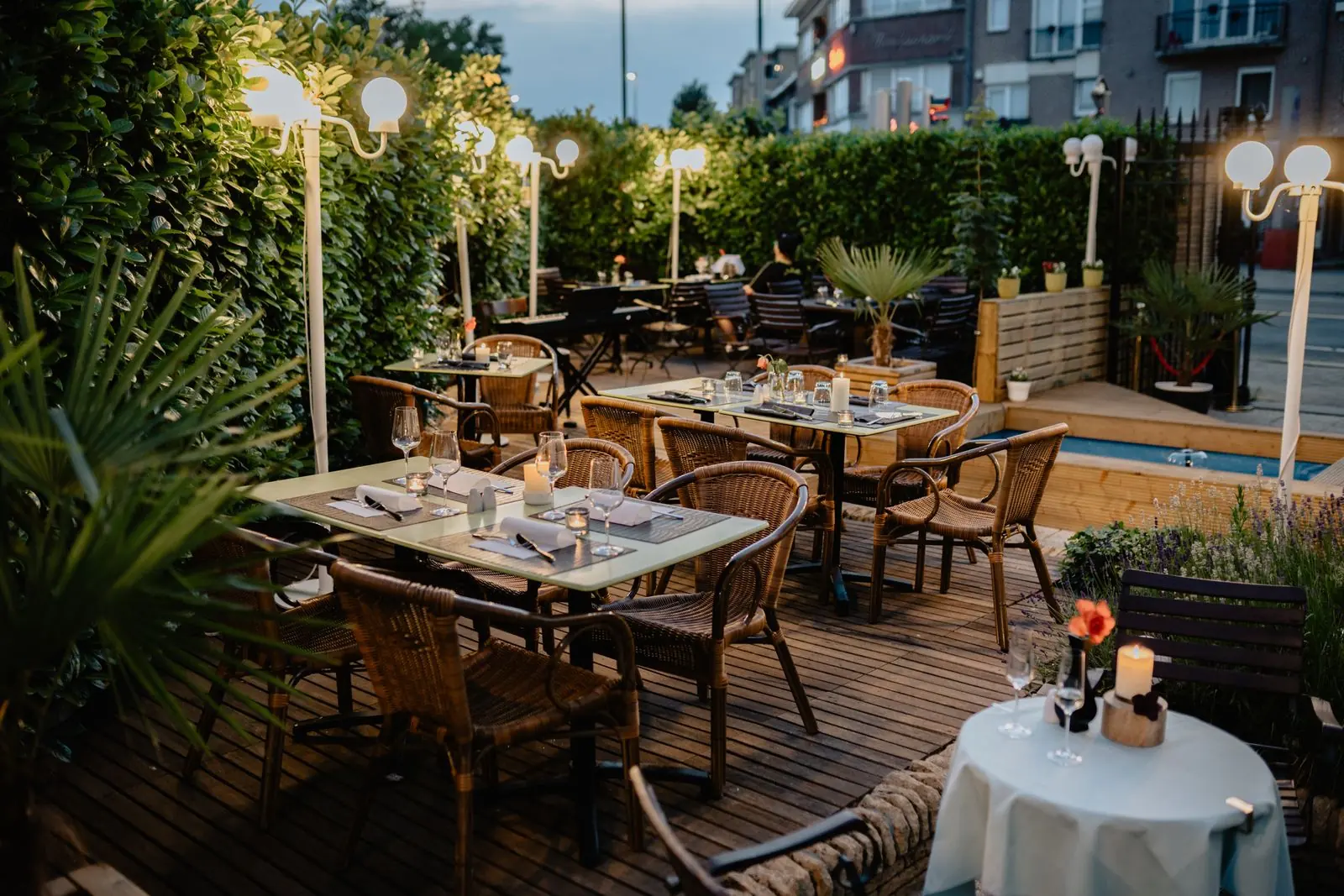 An outdoor restaurant courtyard with tables, plants and string lights at dusk