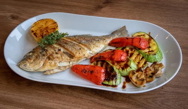 A whole grilled fish with roasted vegetables and lemon
