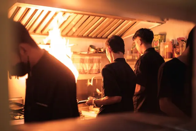 Chefs cooking over a flaring stove in a busy kitchen