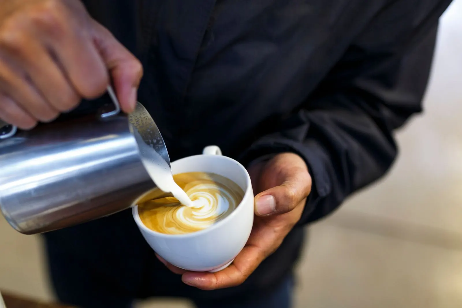 A barista pouring steamed milk into a cup of coffee