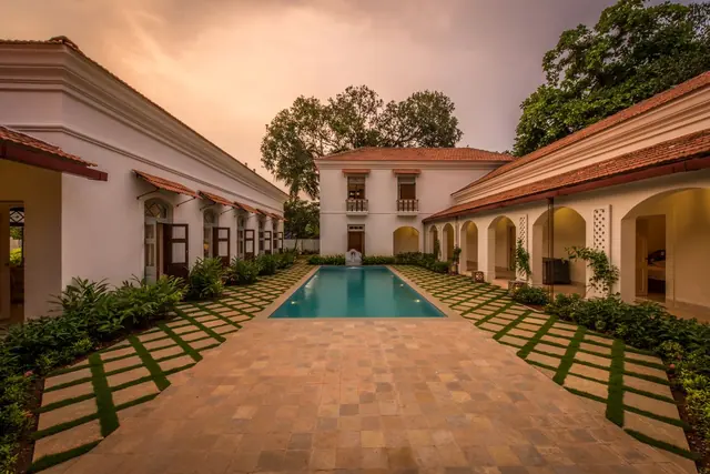 A long narrow pool between arcaded white buildings and lawns at sunset