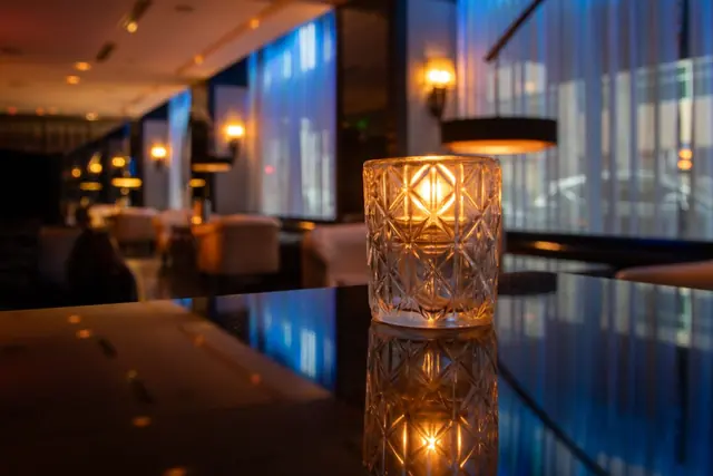 A candle glowing in a cut-glass holder on a polished table in a softly lit lounge