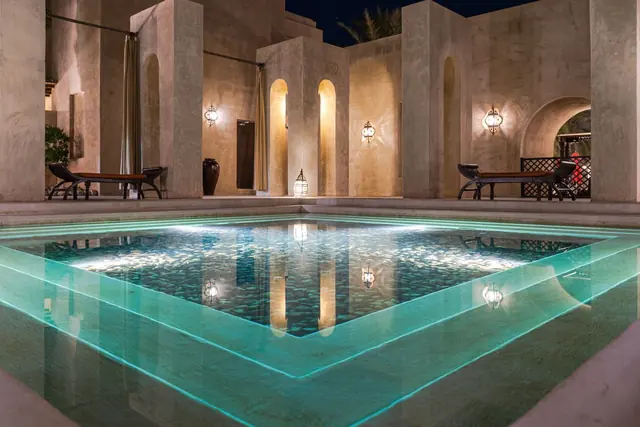 A softly lit pool in a courtyard of arches and lanterns at night