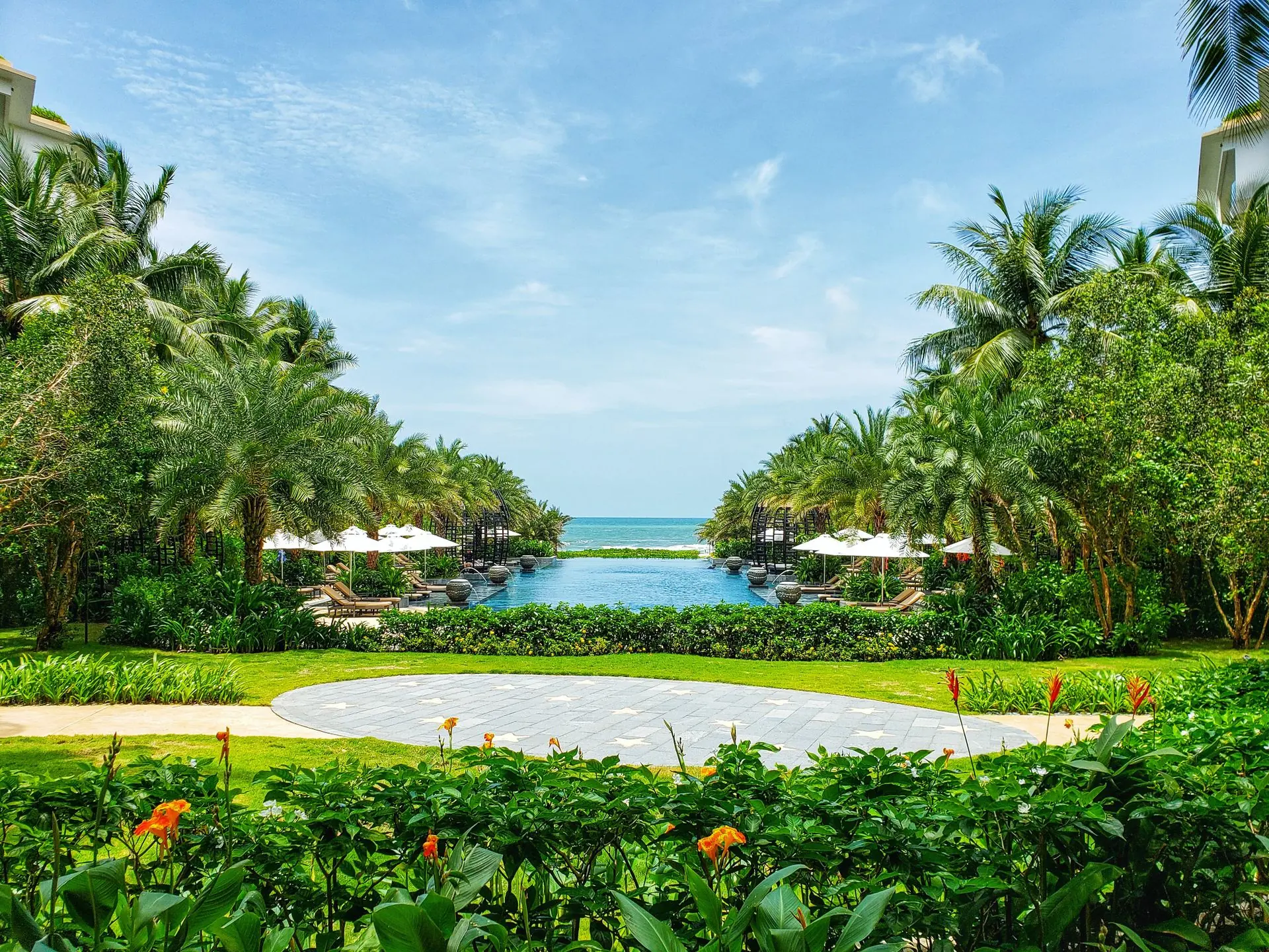An infinity pool framed by palms and lawns, opening onto the sea under a clear sky