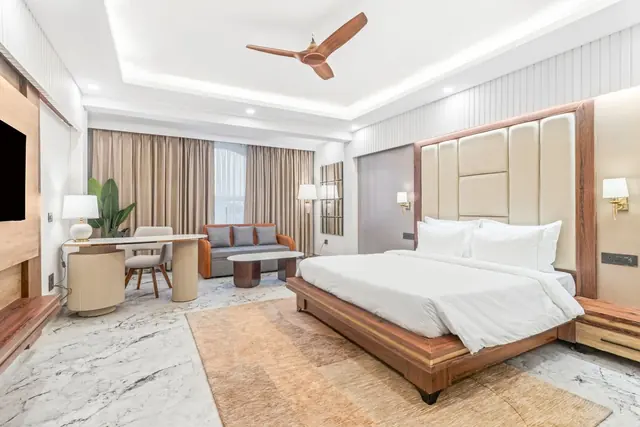 A spacious suite with a padded headboard, a marble floor, a writing desk and a separate sofa corner