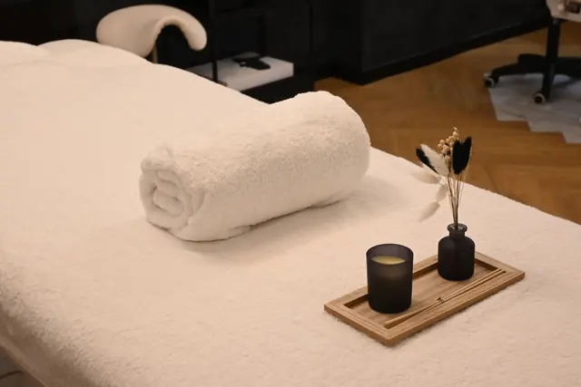 A massage table laid with a rolled white towel, a candle and a small vase of dried flowers