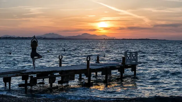A silhouetted figure holding a yoga balance pose at the end of a jetty at sunset