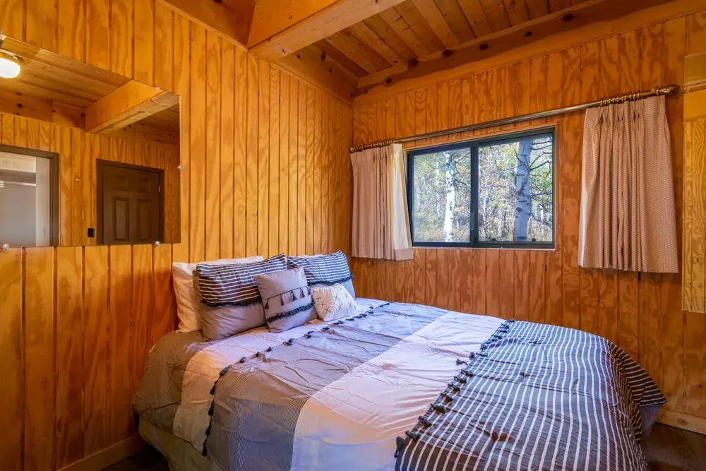 Warm wooden cottage bedroom with a bed and a window looking towards trees