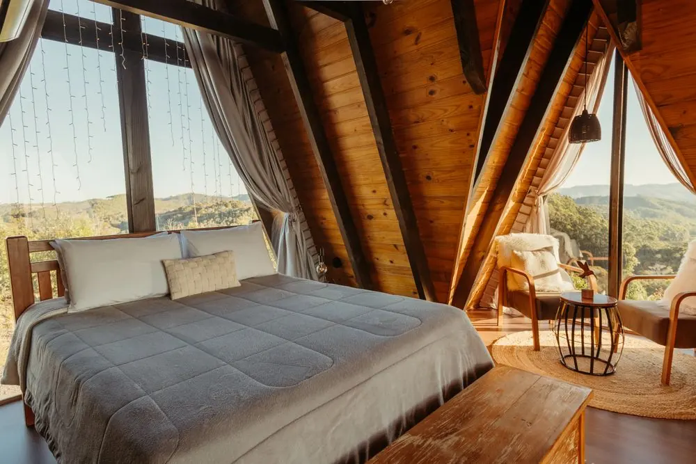 Spacious timber A-frame bedroom with a double bed, chairs and a mountain view
