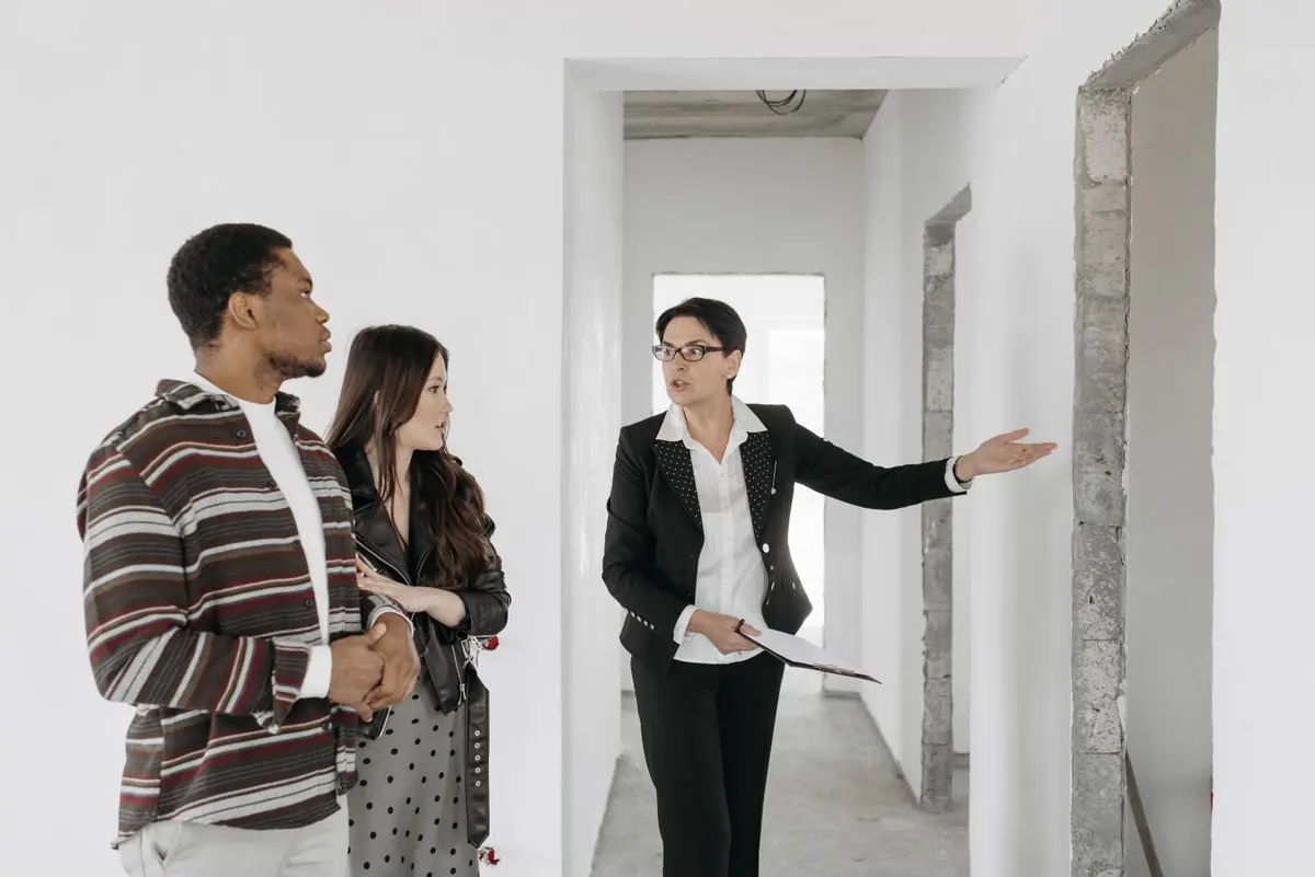An agent showing a couple around an empty, freshly painted apartment and pointing towards a doorway