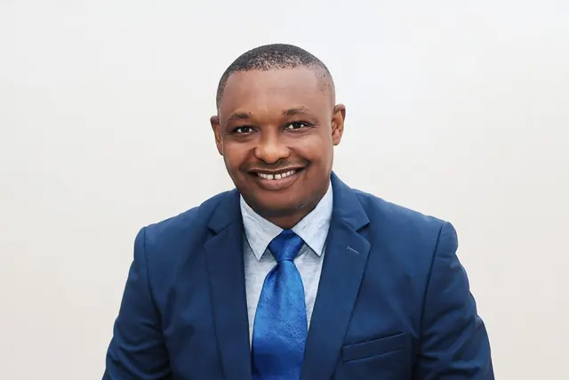 Portrait of a smiling professional in a navy suit and blue tie against a white wall