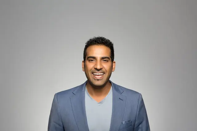 Portrait of a smiling professional in a grey blazer against a pale grey backdrop