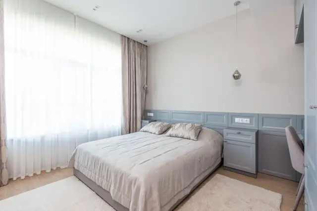 A calm bedroom with a made bed, sheer curtains and pale grey walls