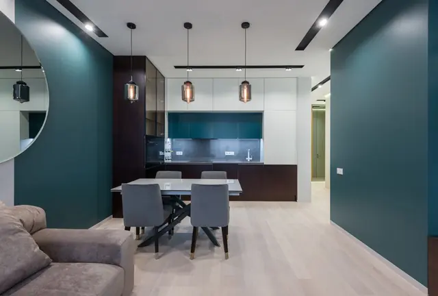An open-plan dining area with pendant lights, a dark teal wall and a kitchen beyond