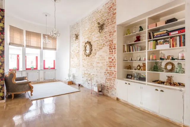 A loft living room with an exposed brick wall, built-in white bookshelves and tall windows