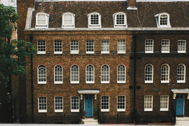 A terrace of tall brick townhouses with white sash windows and blue front doors