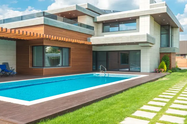 A two-storey modern house with timber and stone cladding beside a long pool and lawn