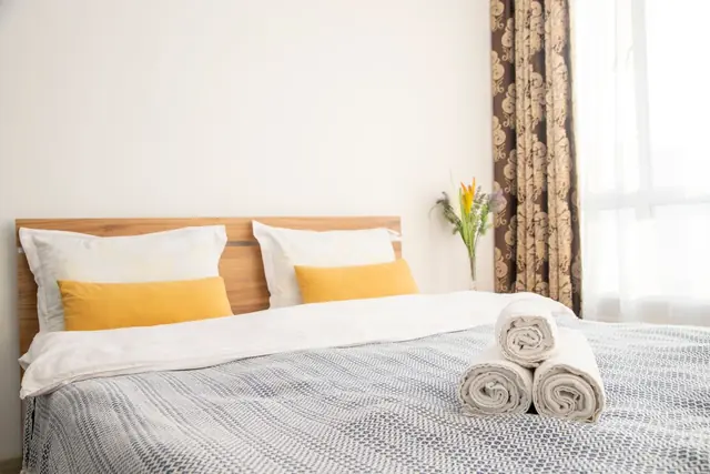 A neatly made bed with folded towels and yellow cushions