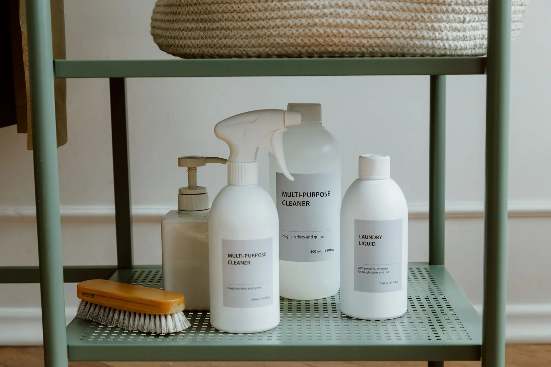 Neatly arranged cleaning bottles and a brush on a pale green shelf