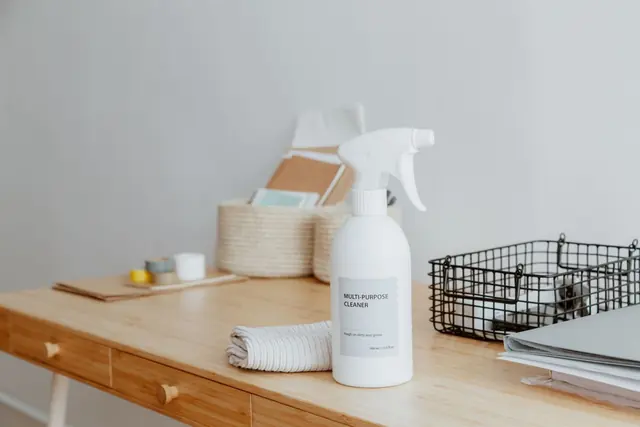A tidy wooden desk with a spray bottle and storage baskets