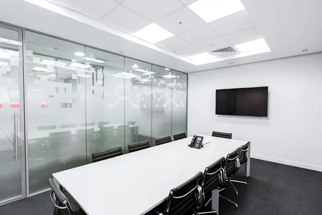 An empty meeting room with a long white table, black chairs and frosted glass walls