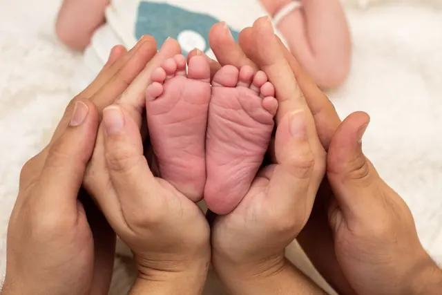 Two pairs of adult hands gently cradling a newborn baby’s feet