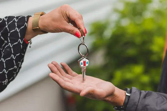 One hand drops a house key on a small house-shaped key ring into another open hand