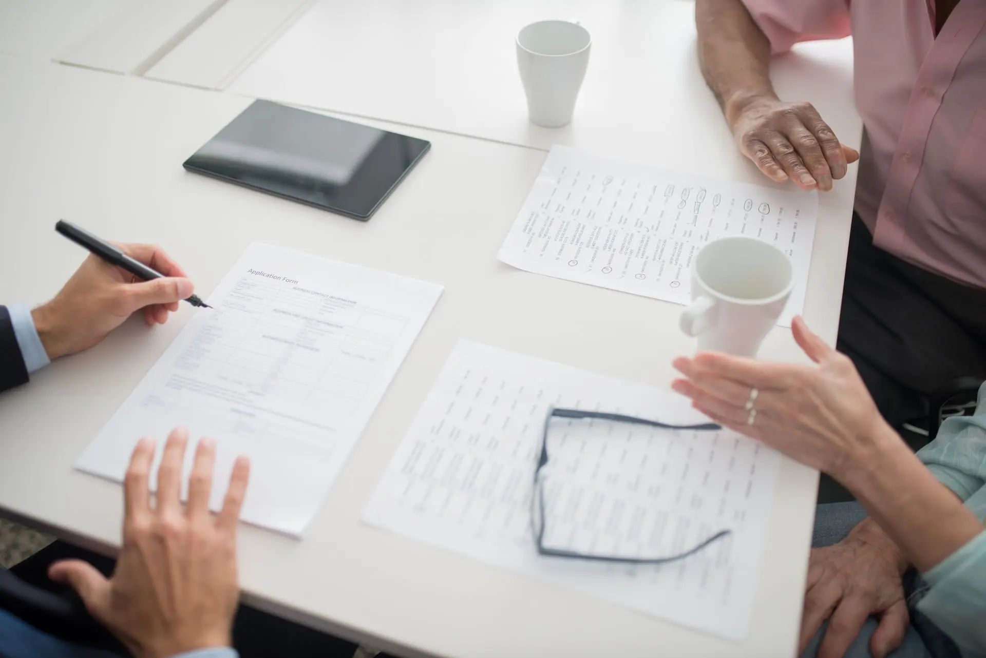 Hands over printed policy pages, a pen and reading glasses on a white table during a meeting