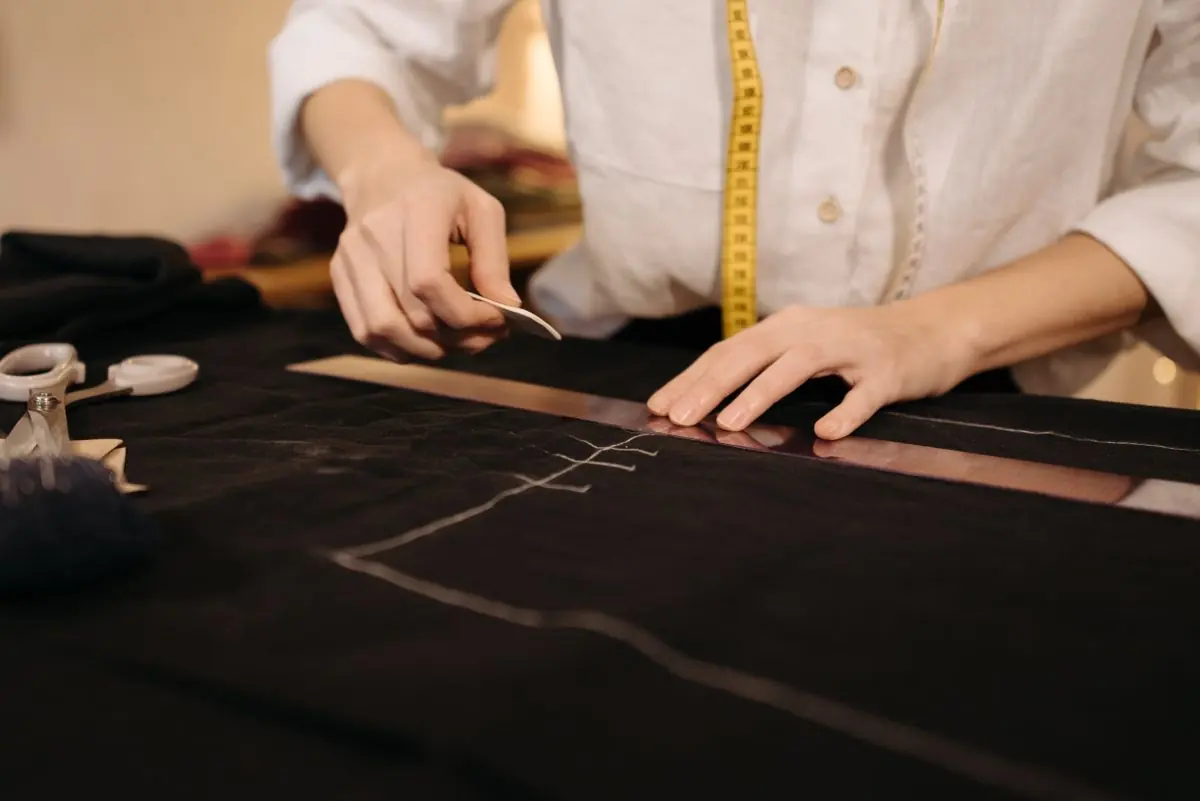 Hands measuring and marking dark fabric on a cutting table