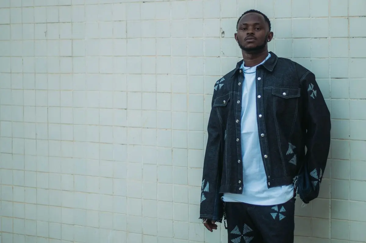 A person in a dark denim jacket standing against pale tiles