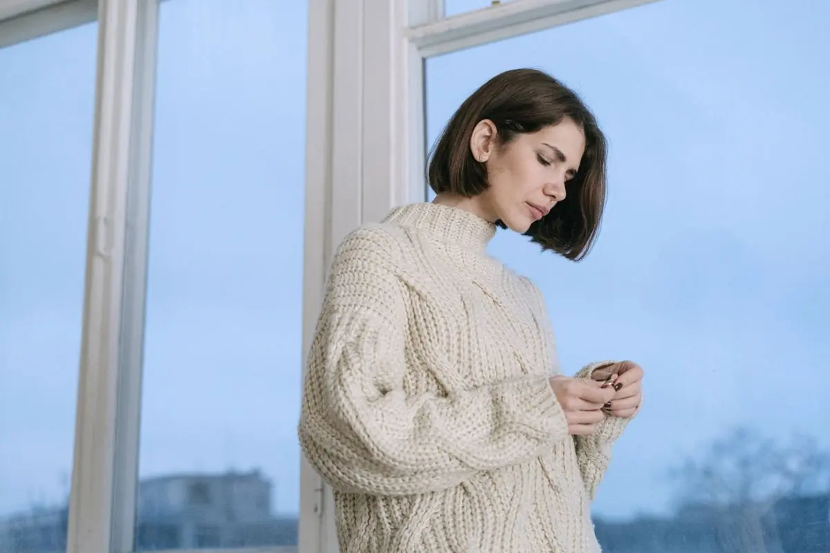 A model in a cream cable-knit sweater by a bright window