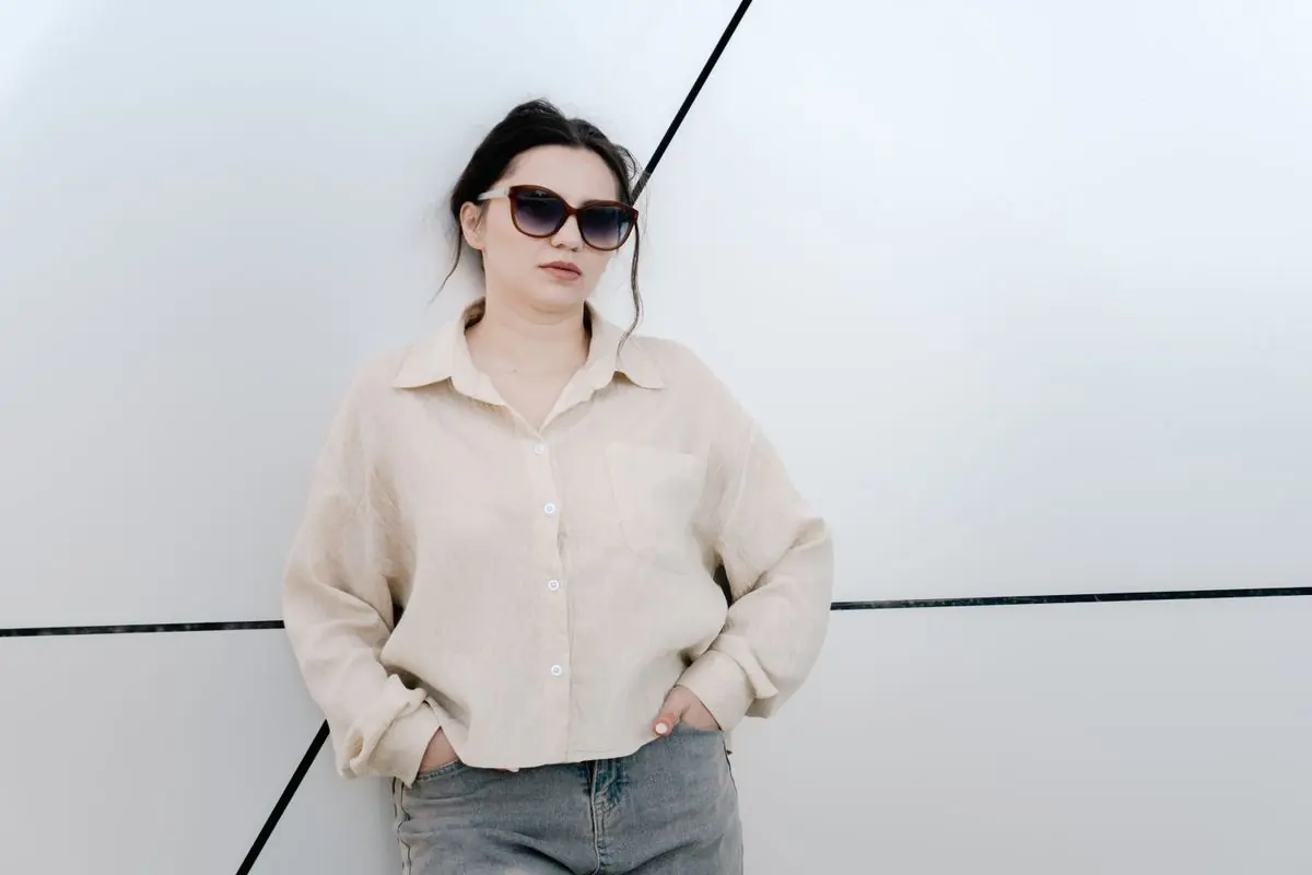 A model in a cream linen shirt and grey trousers against a white wall