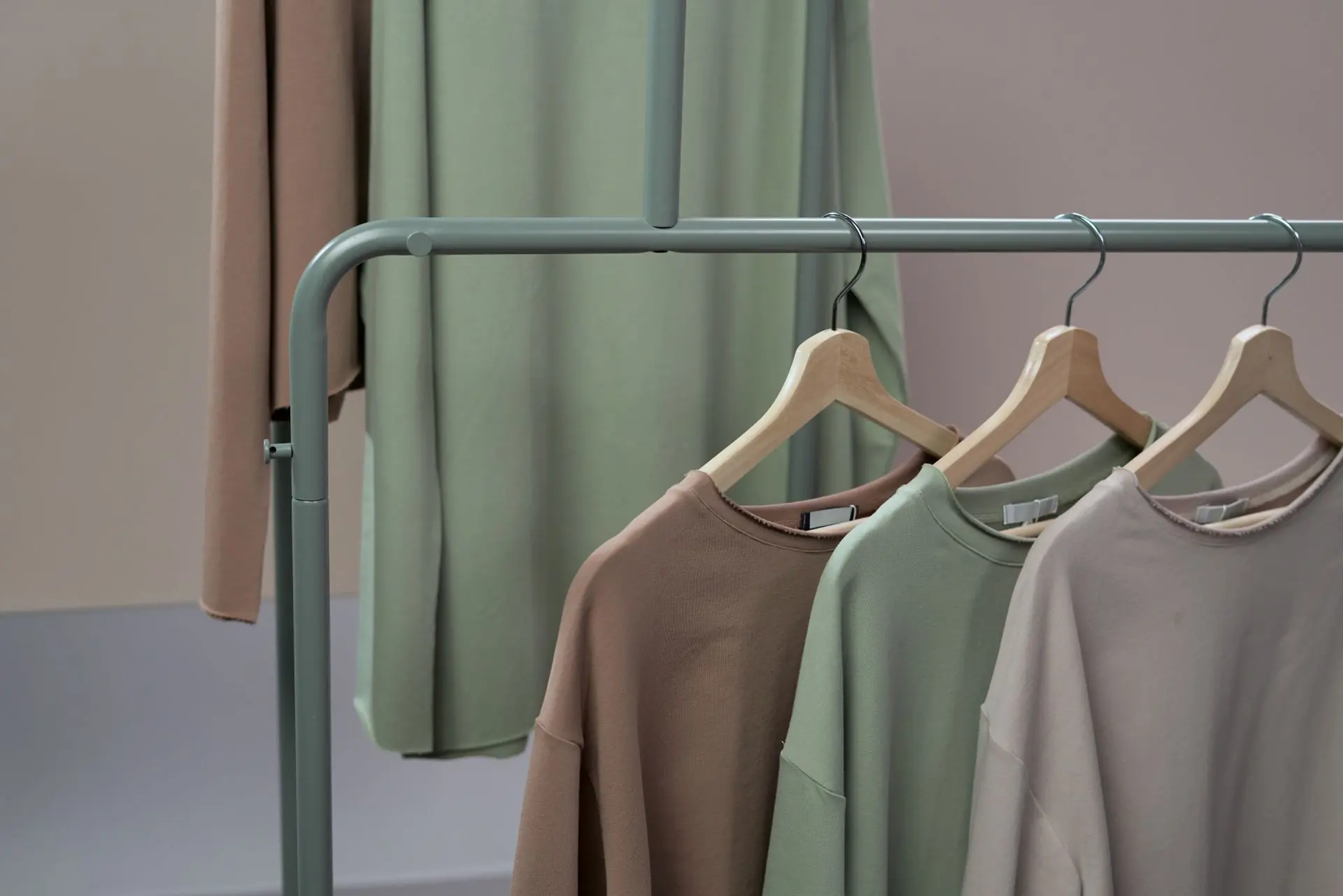 Olive, beige and dusty-pink tops hanging on a sage clothing rail